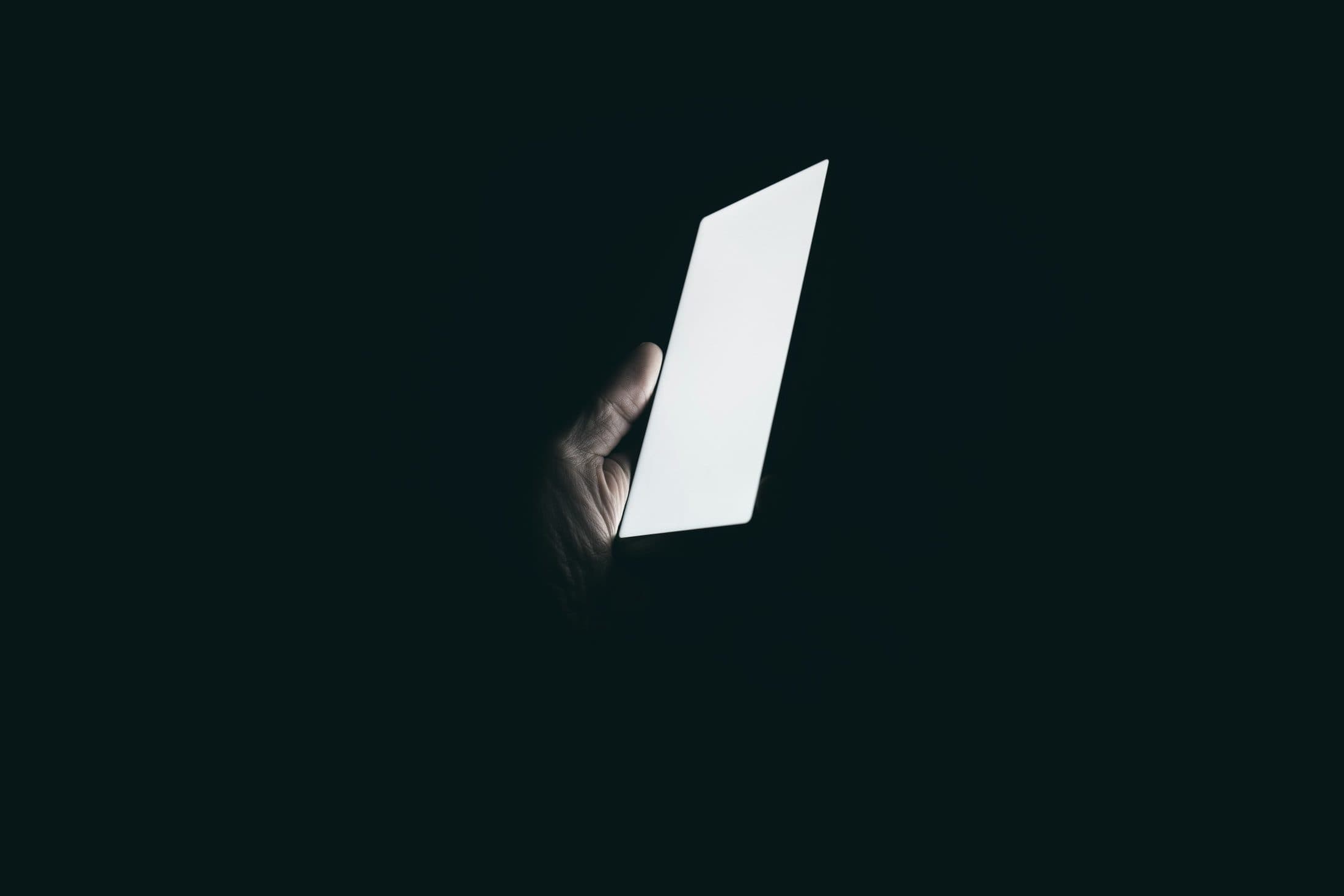 A hand holding a lit phone in the dark